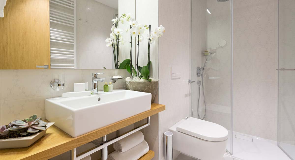 A small, light-colored bathroom with a compact vanity, toilet, and a standing shower illustrate what a beautiful basement bathroom in Kansas City can look like when created by Karin Ross Designs.