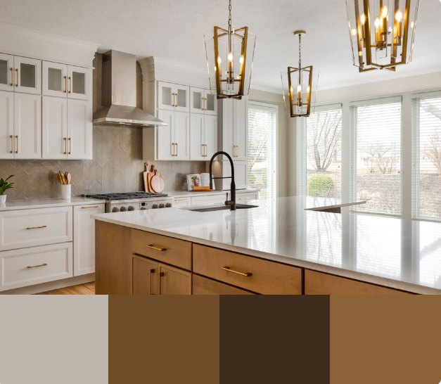 A modern kitchen with white cabinets, a large island with a white countertop, and a gold faucet. The backsplash is a light grey marble, and the floor is a light brown wood.