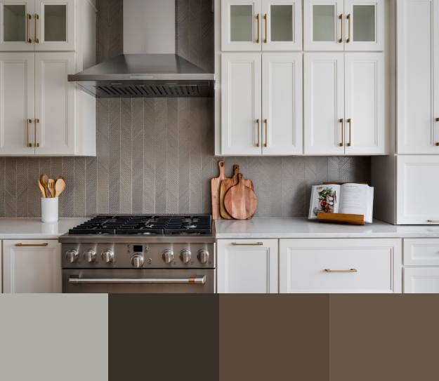 A modern kitchen with white cabinets and gold hardware. The countertop is a light gray marble with a waterfall edge. The backsplash is a neutral gray stone with a vertical pattern. A stainless steel range and hood are centered on the countertop.