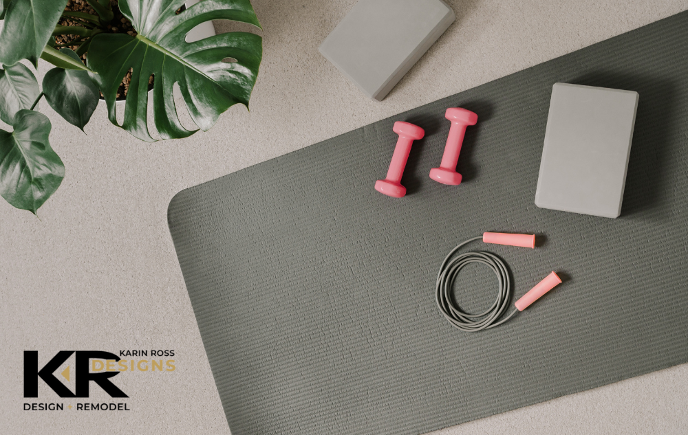 Basic home gym equipment, such as a yoga mat, a jump rope, yoga blocks, and weights, are laying on the floor. In the top left corner is a healthy plant. In the bottom left corner is the Karin Ross Designs logo. This indicates that the piece will discuss creating a basement home gym with Karin Ross Designs.