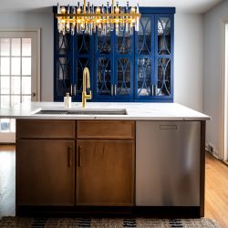 Brown wood kitchen island with a dishwasher and marble countertops. A blue china cabinet is behind the island.